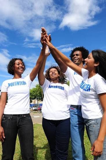 Volunteers in matching shirts celebrating together with a group high-five outdoors