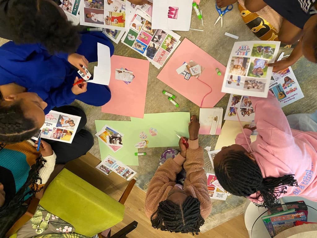 An overhead view of girls and young women arranging photos, paper, and glue during a workshop